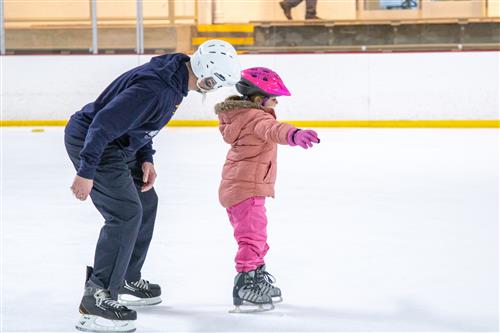 Teacher helping young student ice skate
